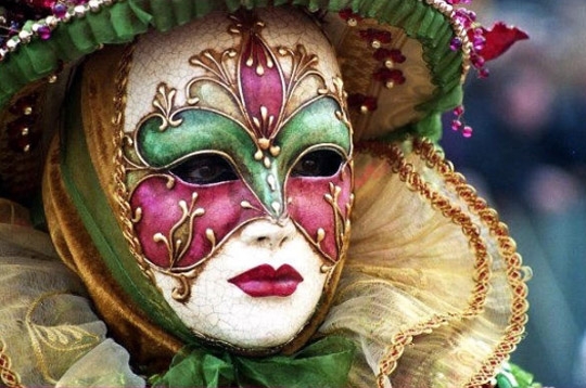 Masque de carnaval porté représentant une personne avec des couleurs vertes, violettes et blanches. On distingue les yeux du porteur à travers les trous du masque.