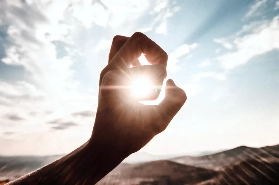 Doigts d'une main encerclant le soleil. Les rayons du soleil passent entre les doigts symbolisant le Soleil en astrologie.