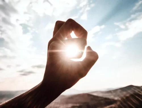 Doigts d'une main encerclant le soleil. Les rayons du soleil passent entre les doigts symbolisant le Soleil en astrologie.
