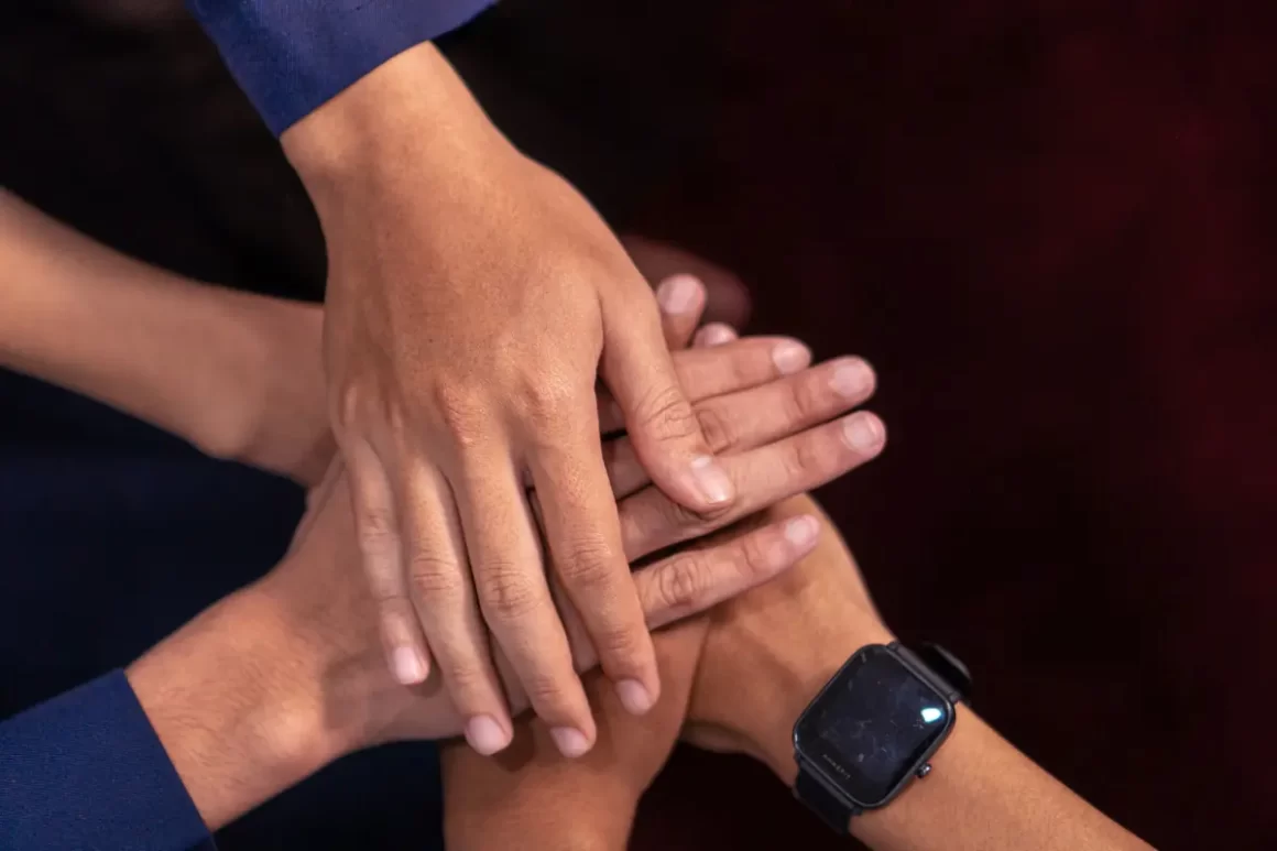 Plusieurs personnes superposent leurs mains dans un geste d’engagement collectif.