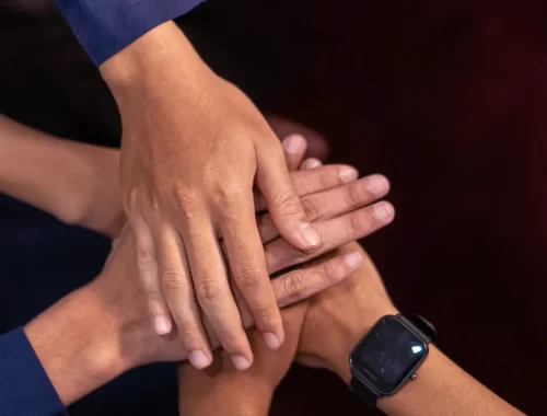 Plusieurs personnes superposent leurs mains dans un geste d’engagement collectif.